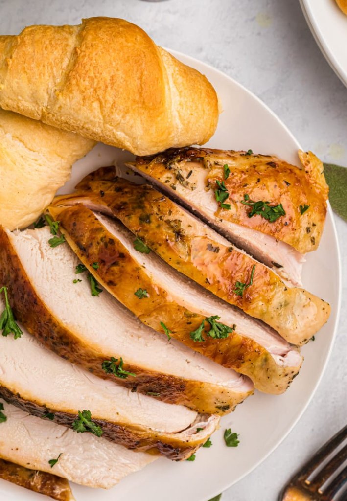 sliced roasted turkey on a white plate with a roll