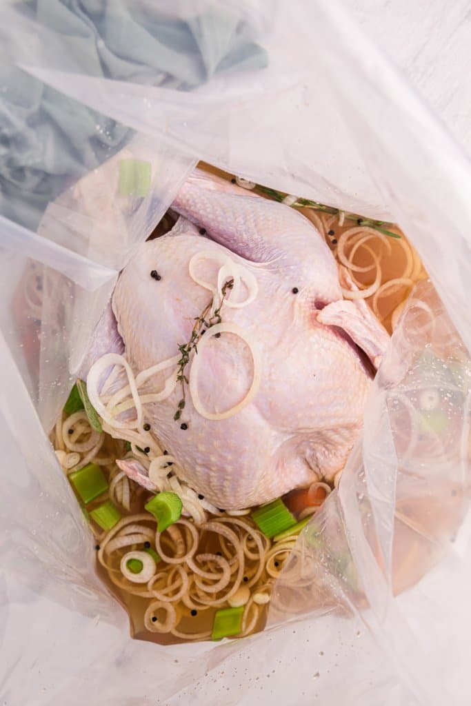 uncooked turkey in a brine bag with broth and vegetables