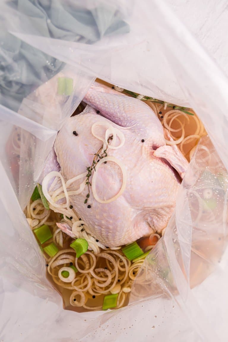 Uncooked turkey in a brine bag with broth and vegetables.