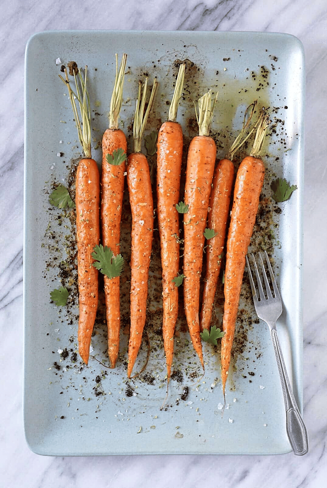 Whole carrots on white serving platter with silver fork.