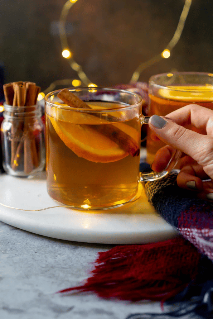hand holding up clear mug of hot toddy with orange