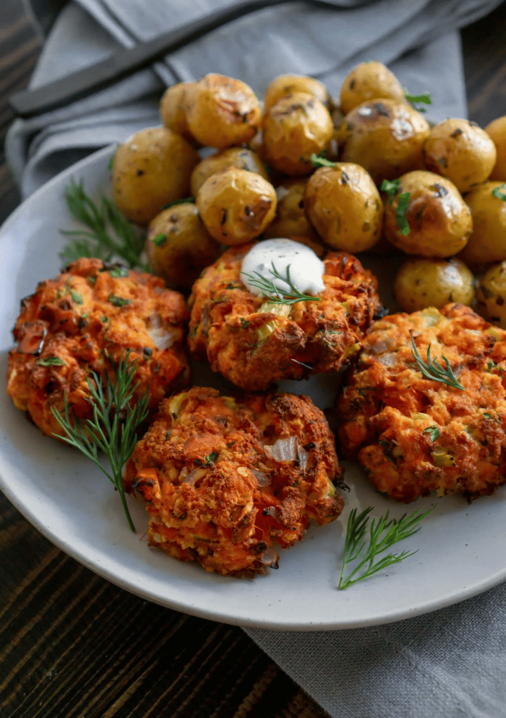 salmon cakes with lemon dill sauce on a white serving plate with baby potatoes in the background 