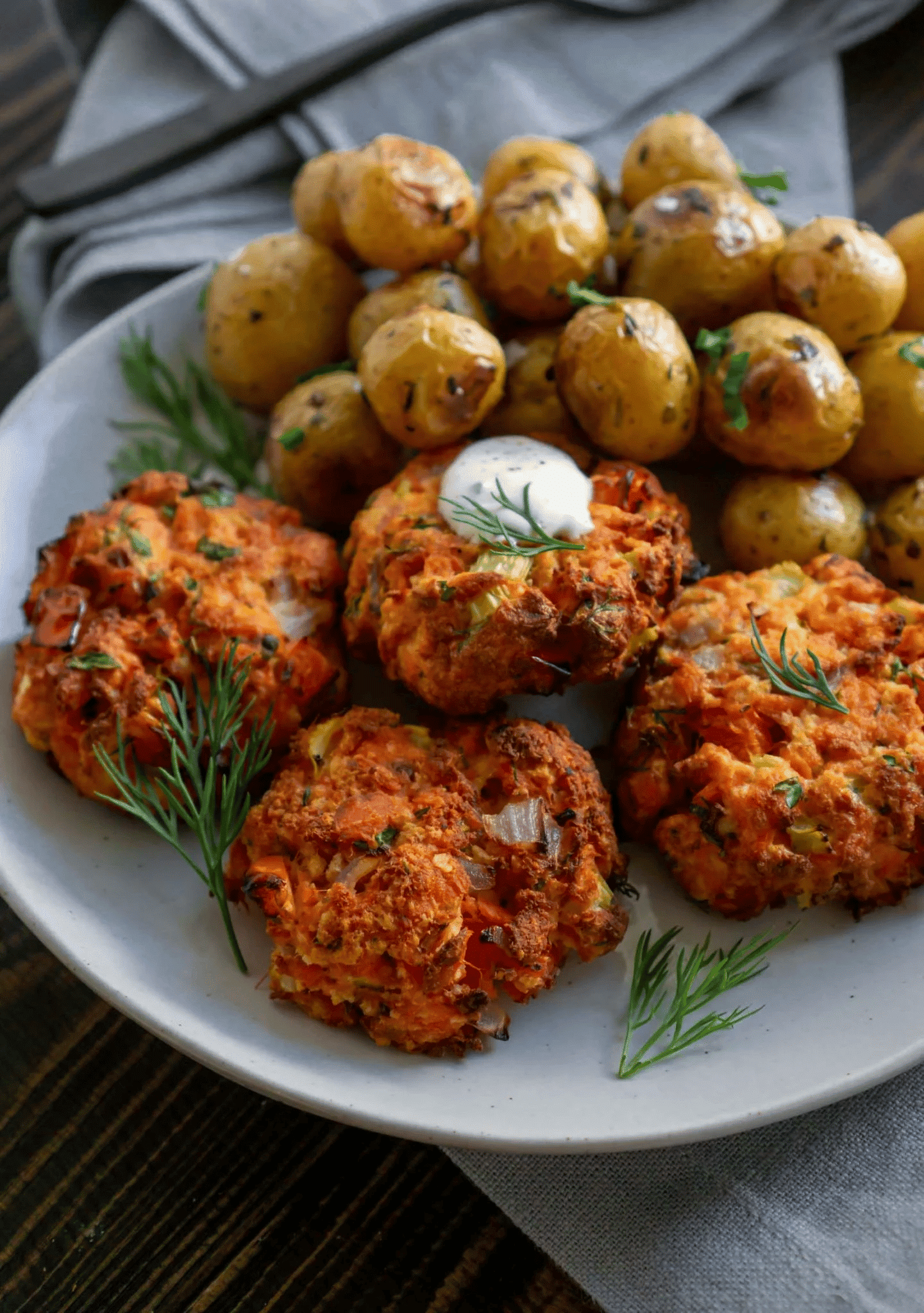 Salmon cakes with lemon dill sauce on a white serving plate with baby potatoes in the background.