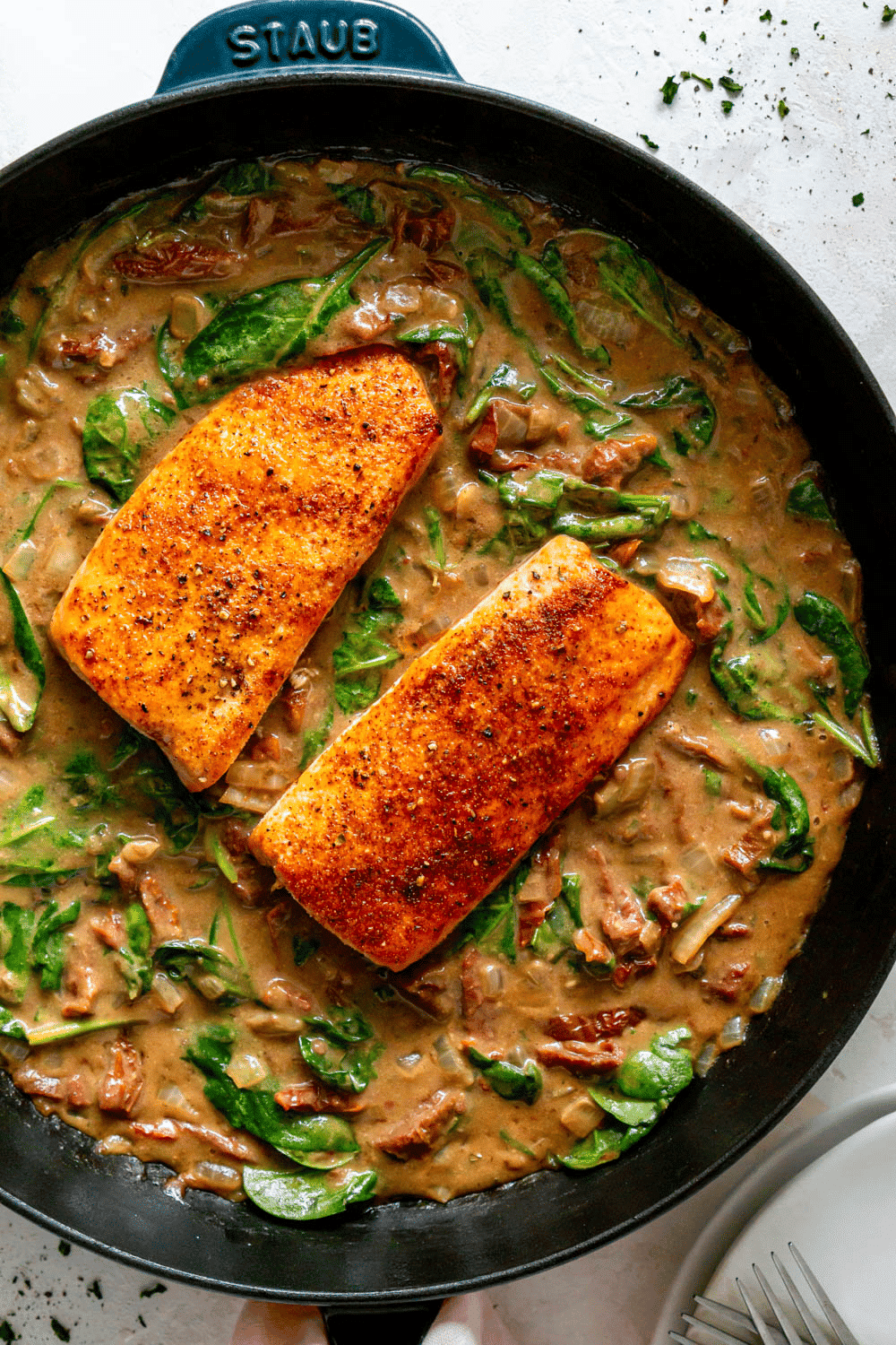 Creamy garlic tuscan salmon in a pan with creamy spinach and sun dried tomatoes.