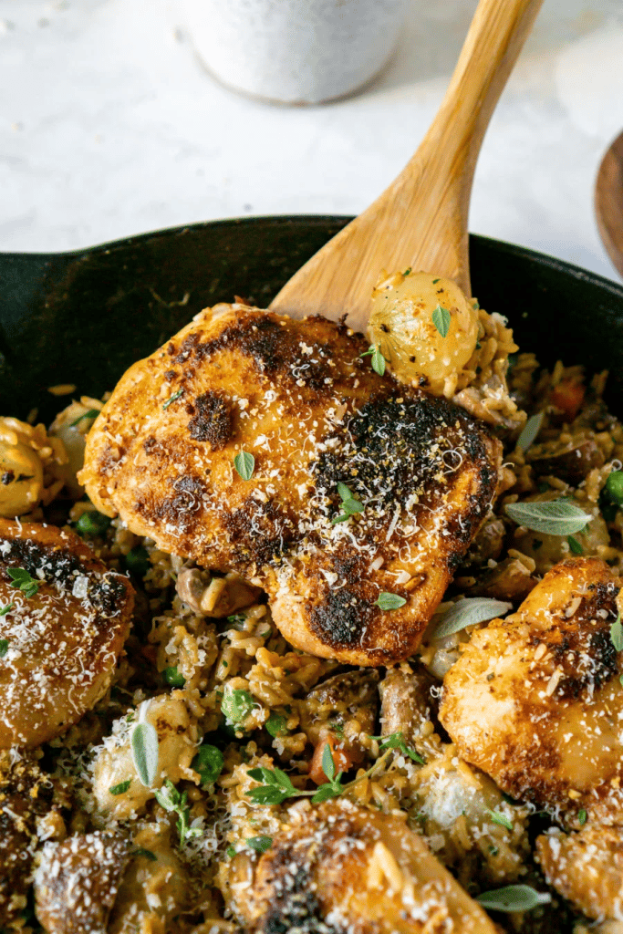 close up of a piece on chicken on a spatula with creamy rice and herbs in the background 