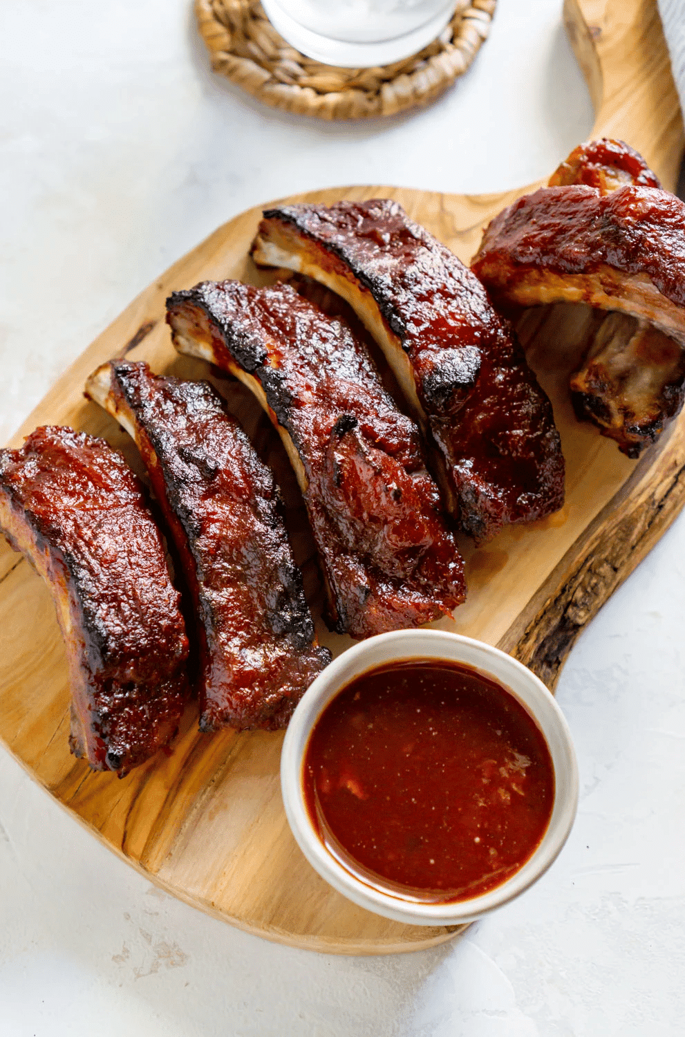 Baby back ribs cut on wood platter with sauce.