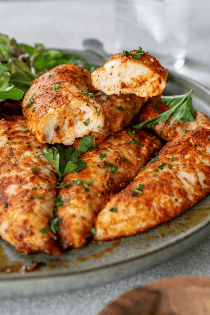 oven baked chicken tenders on serving plate with one split open and herbs 