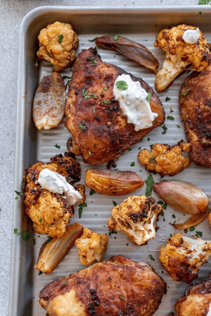 chicken, onions and cauliflower on a baking sheet with herbed yogurt sauce on chicken