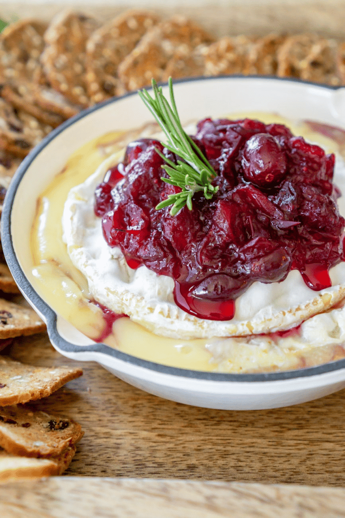 close up of cranberry baked brie in a baking dish with crisps in the background 