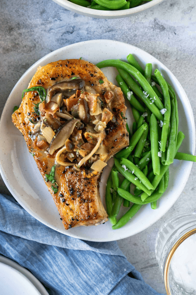 pork chop smothered in mushroom sauce with a side on green beans on white plate