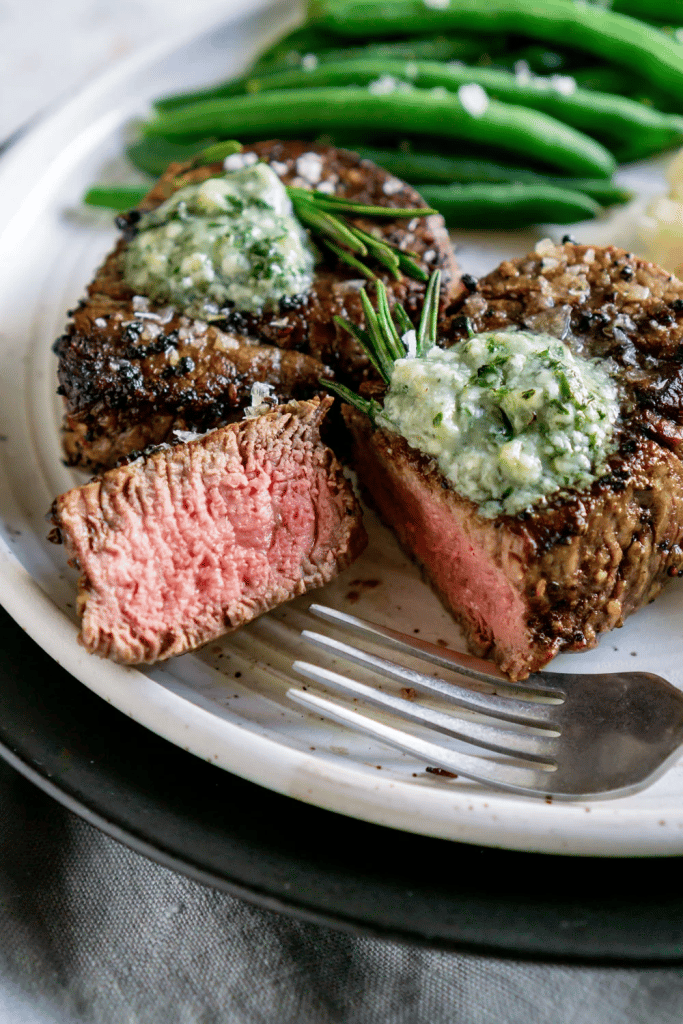 close up of air fryer filet mignon with blue cheese butter on top and green beans in the background 