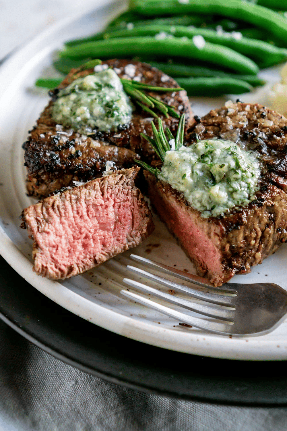 Close up of air fryer filet mignon with blue cheese butter on top and green beans in the background.