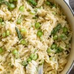 close up of goat cheese orzo pasta salad in a white pot with a serving spoon