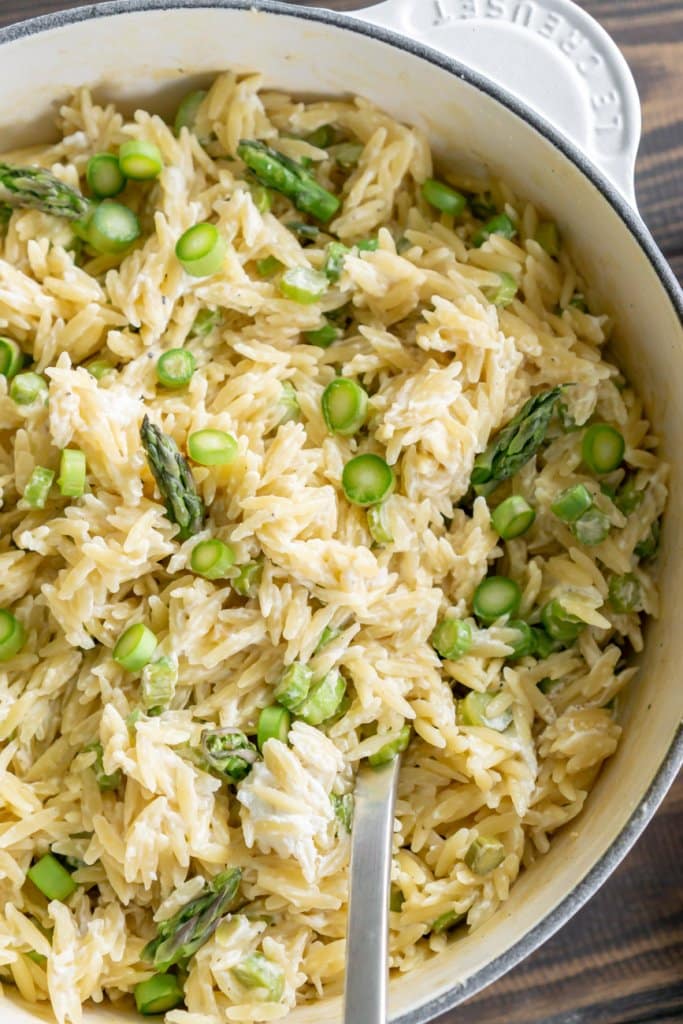 close up of goat cheese orzo pasta salad in a white pot with a serving spoon