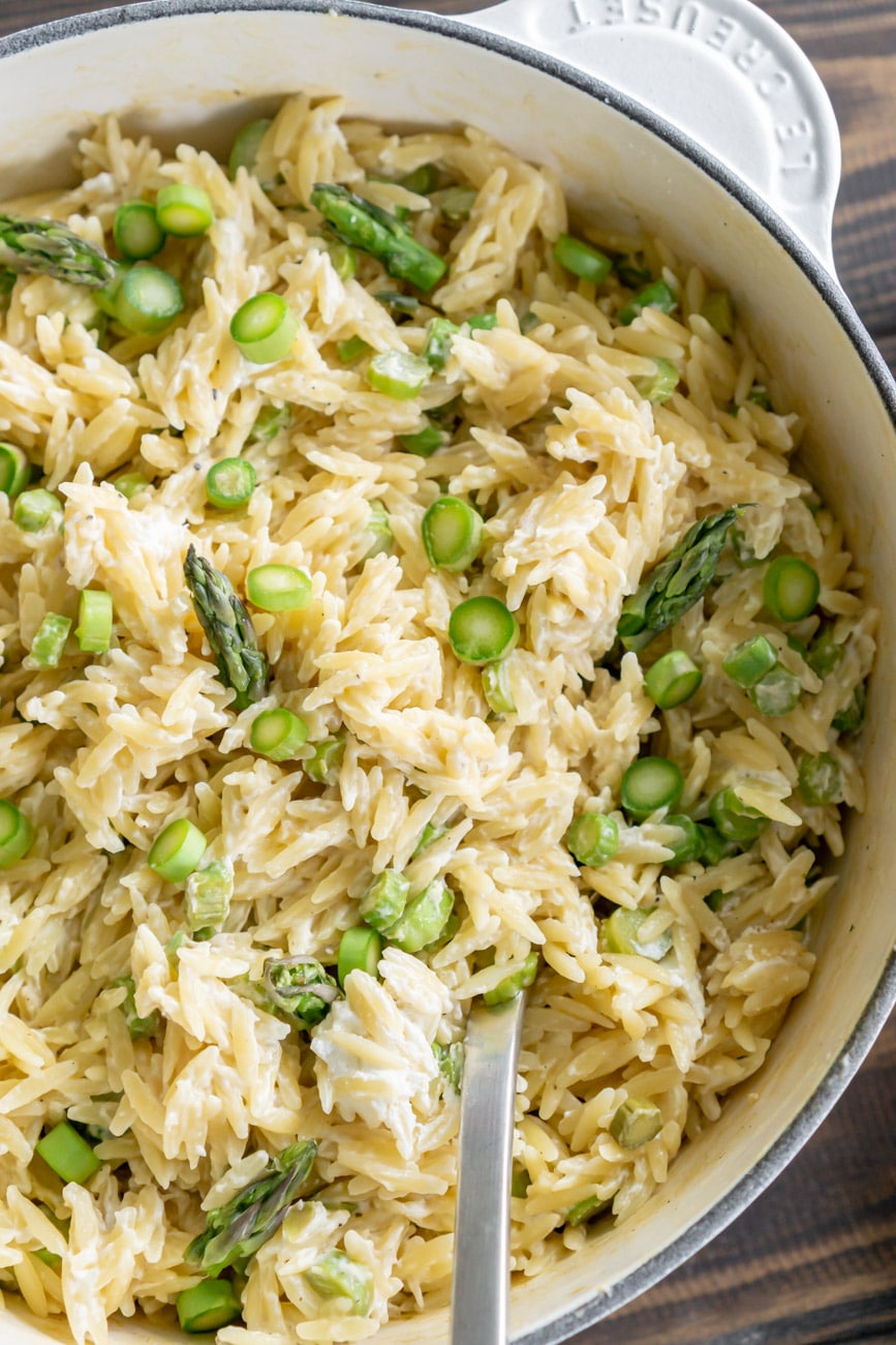 Close up of goat cheese orzo pasta salad in a white pot with a serving spoon.