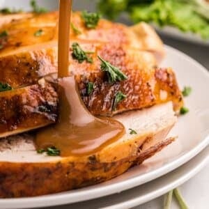 pouring gravy over sliced roasted turkey.