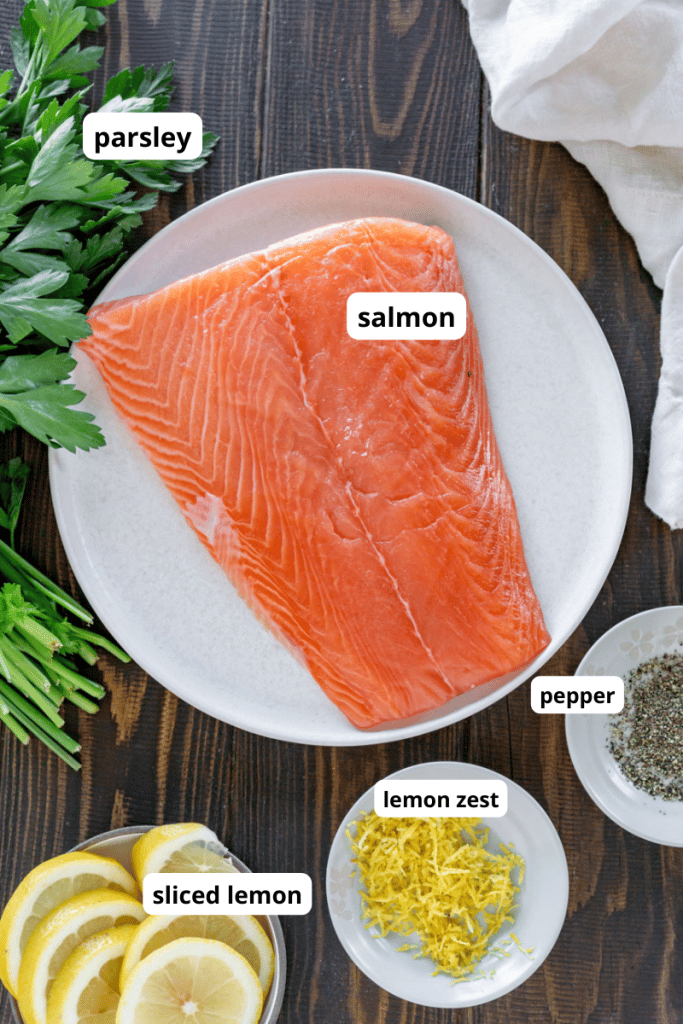 salmon on a plate, sliced lemon, black pepper, lemon zest, and parsley