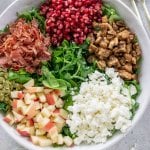 a bowl of lettuce with pomegranate, feta cheese, apples, prosciutto, and walnuts