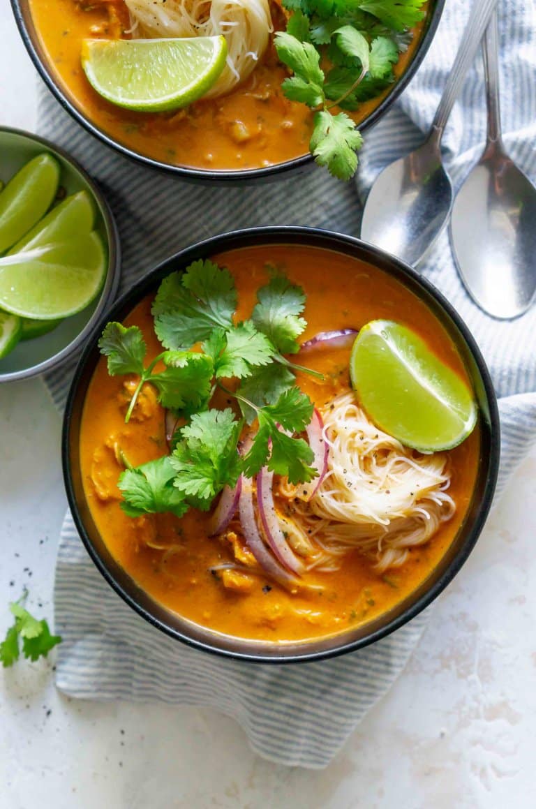 two black bowls of coconut curry chicken soup with onions, cilantro, and lime wedges