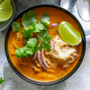 a black bowl of coconut curry chicken soup with onions, cilantro, and lime wedgesurry chicken soup