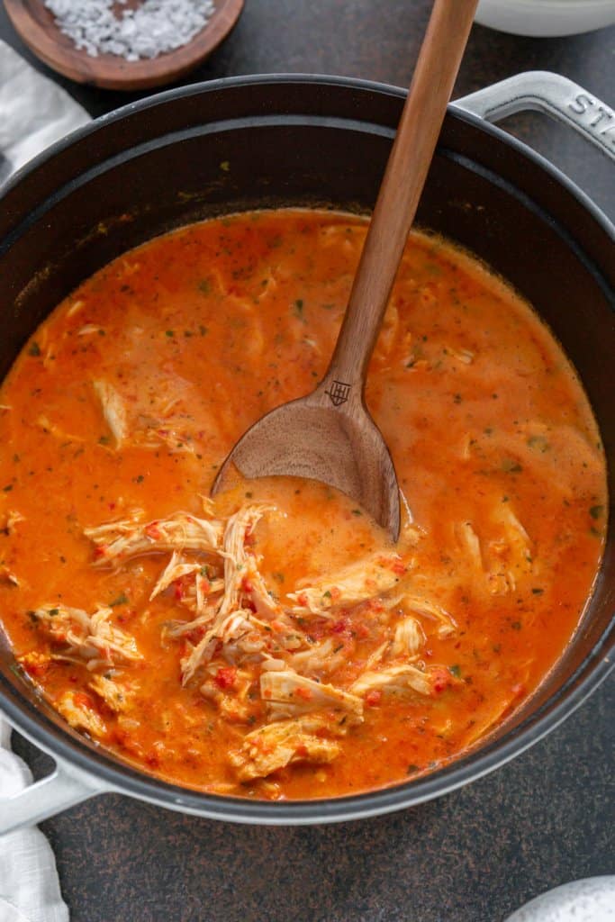 a big soup pot of roasted red pepper soup with a wooden spoon