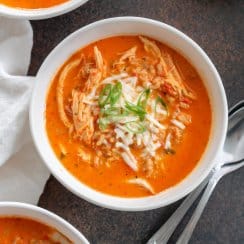three bowls of roasted red pepper soup with two spoons to the side