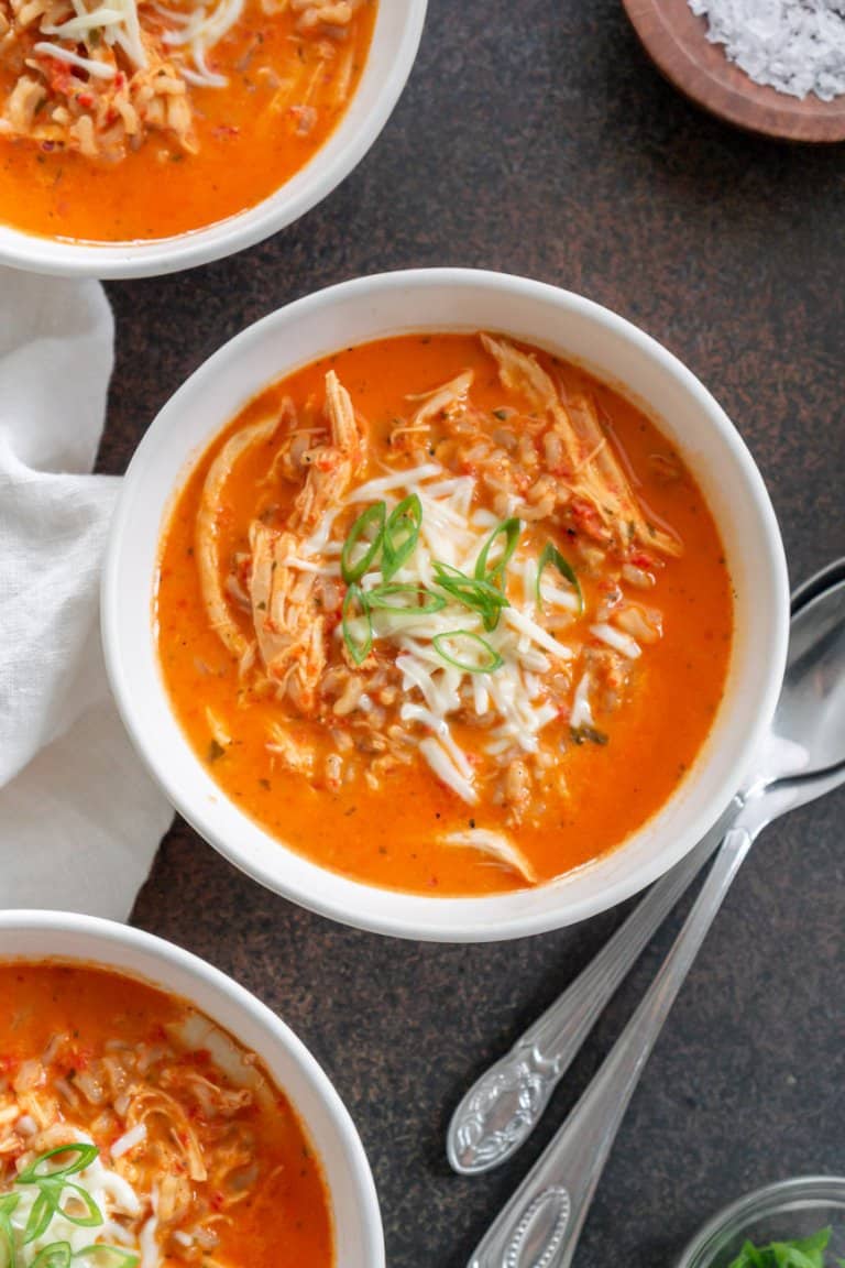 three bowls of roasted red pepper soup with two spoons to the side