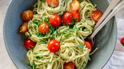 avocado pasta sauce on spaghetti in a bowl with a fork and tomatoes