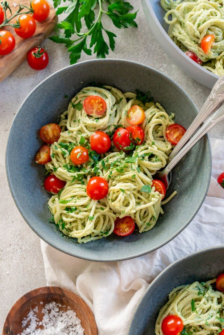 avocado pasta sauce on spaghetti in a bowl with a fork and tomatoes