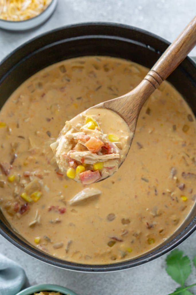 a wooden spoon holding a spoonful of chicken taco soup over a pot