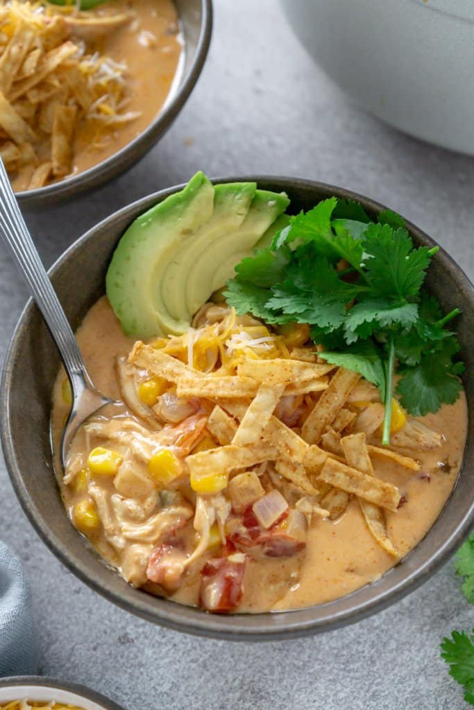 two bowls of chicken taco soup with avocado, cilantro, and tortilla strips on top
