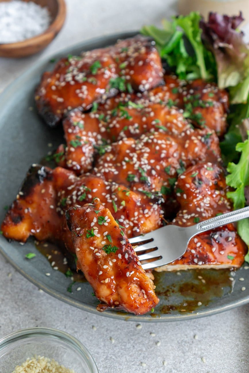 A bite of chicken on a fork with greens on the side.