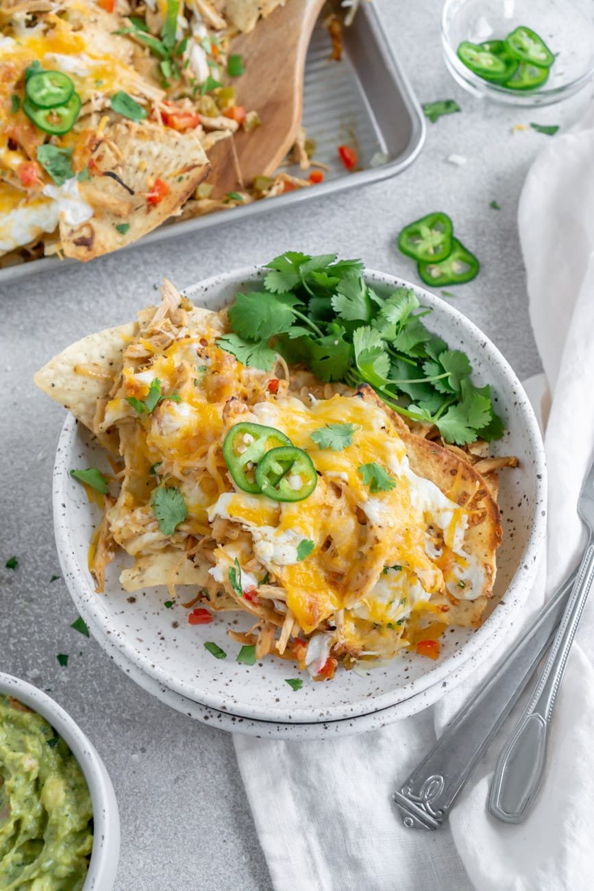 chicken fajita nachos on a white plate with guacamole on the side.