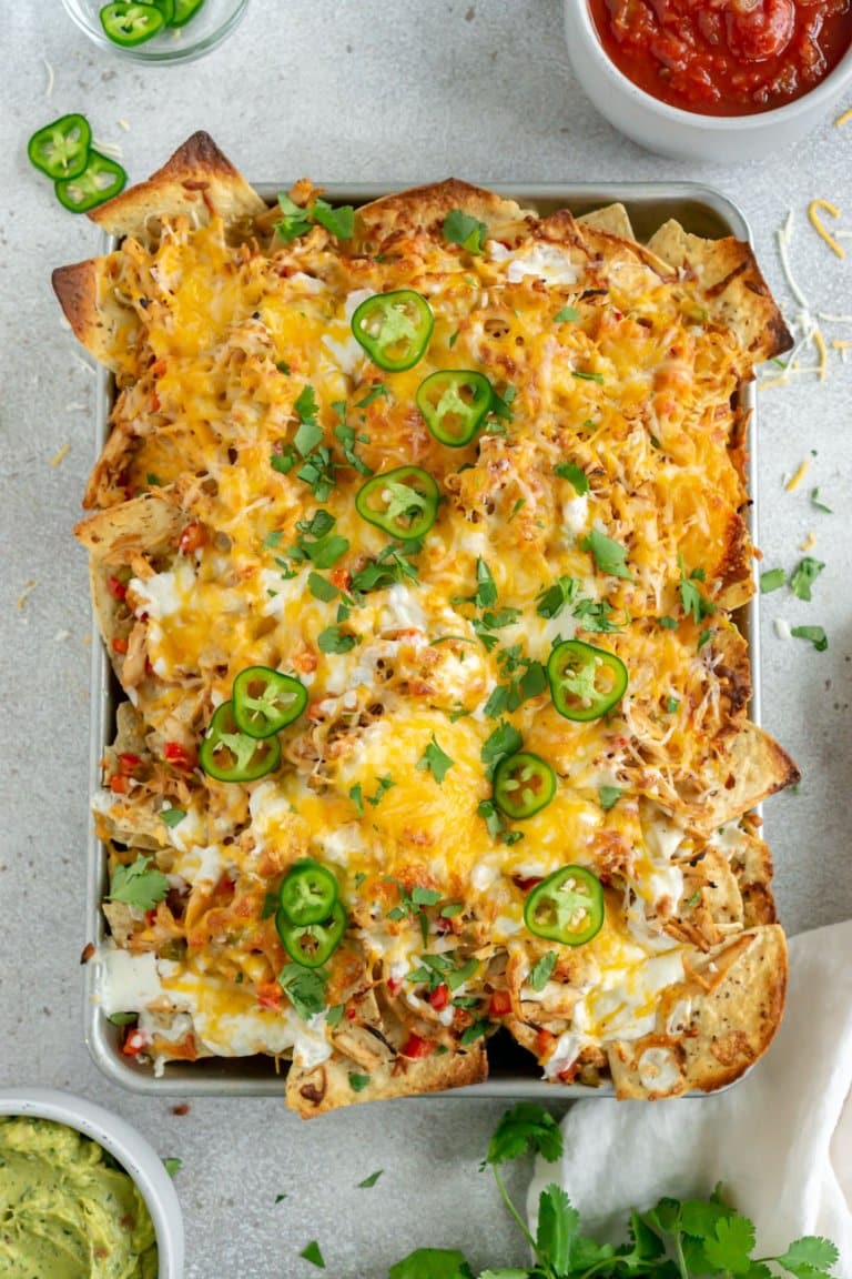 chicken fajitas nachos on a sheet pan with guacamole and salsa on the side.