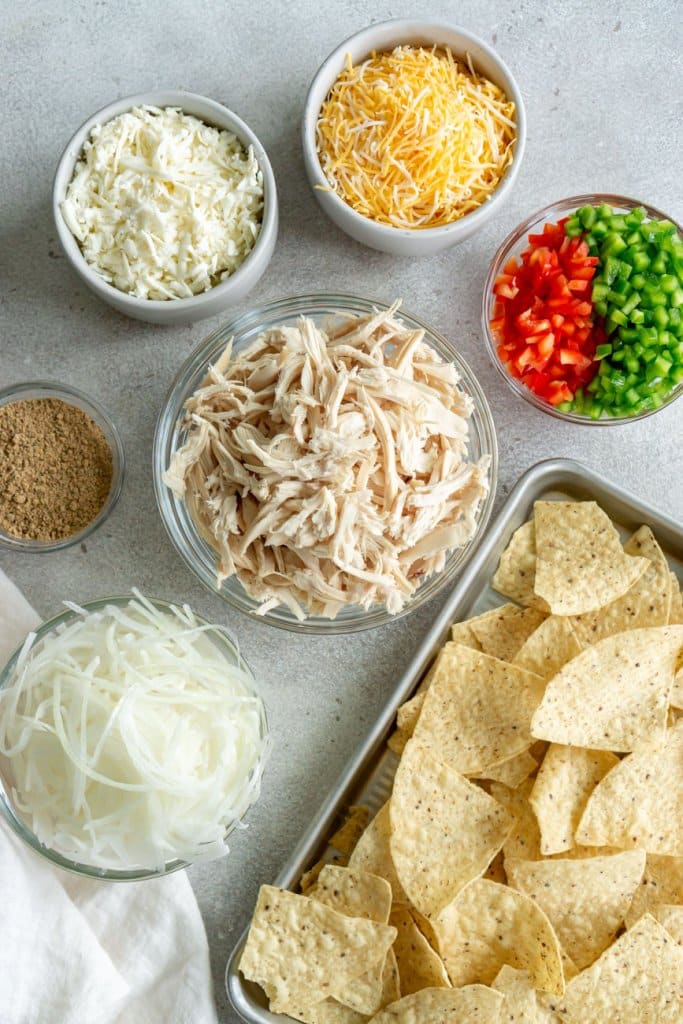 shredded chicken, shredded cheese, diced peppers, tortilla chips, and onions in small bowls