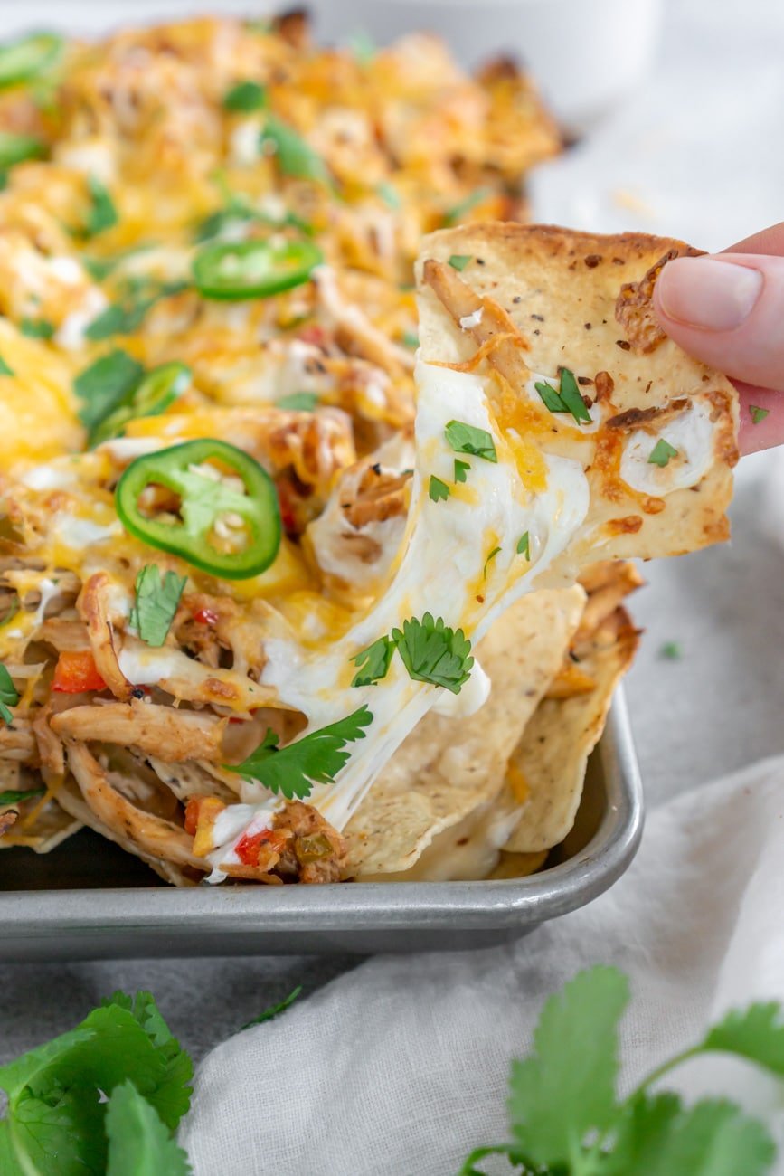 hand grabbing a nacho with lots of cheese on it.