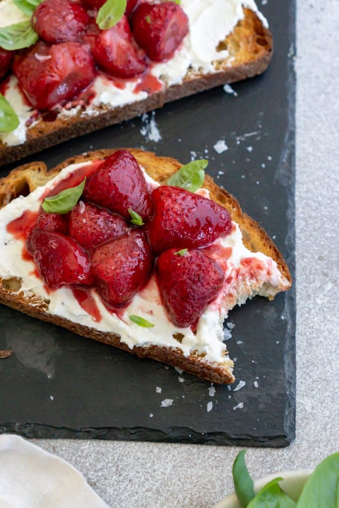 bite taken out of toast with whipped feta and balsamic roasted strawberries