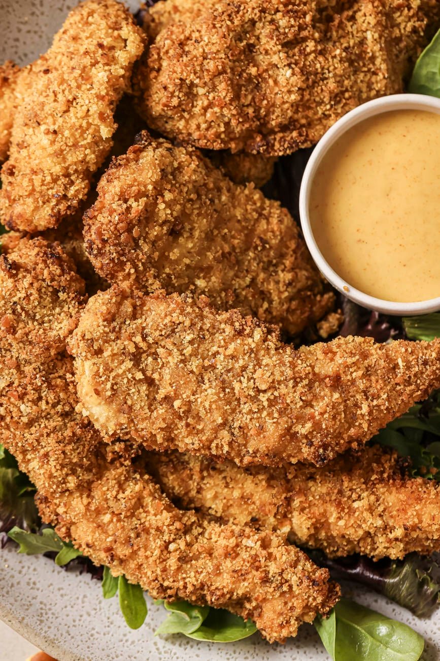 pretzel crusted chicken tenders on a plate with mixed greens and honey mustard sauce.