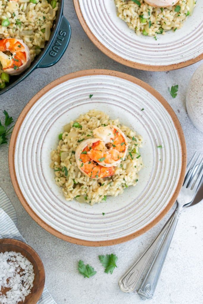 a bowl of risotto with shrimp on top, a fork and another plate and pan to the side
