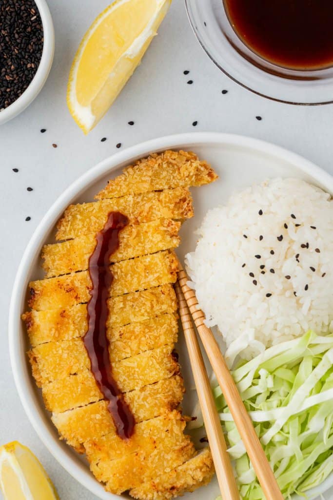 close up of air fryer chicken on a white plate with white rice, chopsticks and black sesame seeds