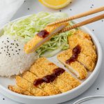 chopsticks holding a piece of chicken over a plate with white rice