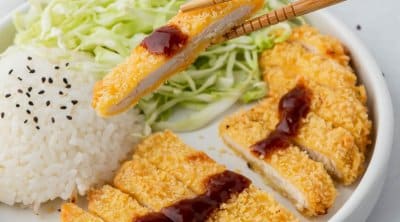 chopsticks holding a piece of chicken over a plate with white rice