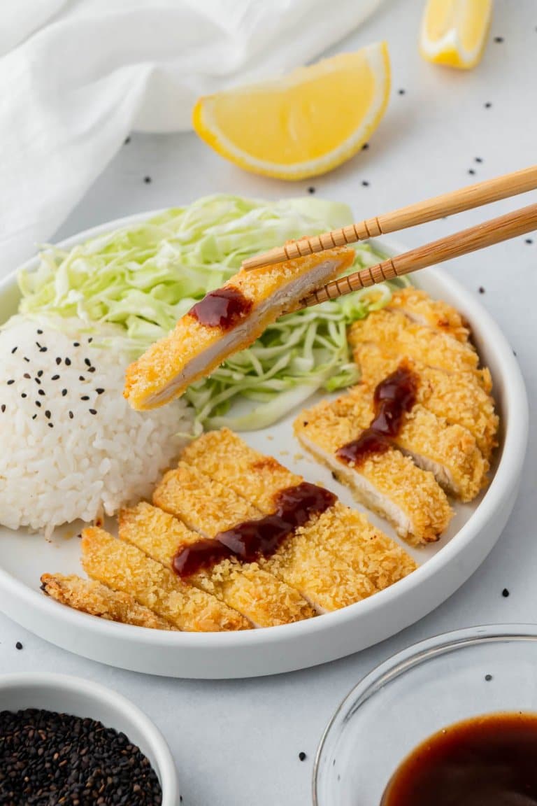 chopsticks holding a piece of chicken over a plate with white rice