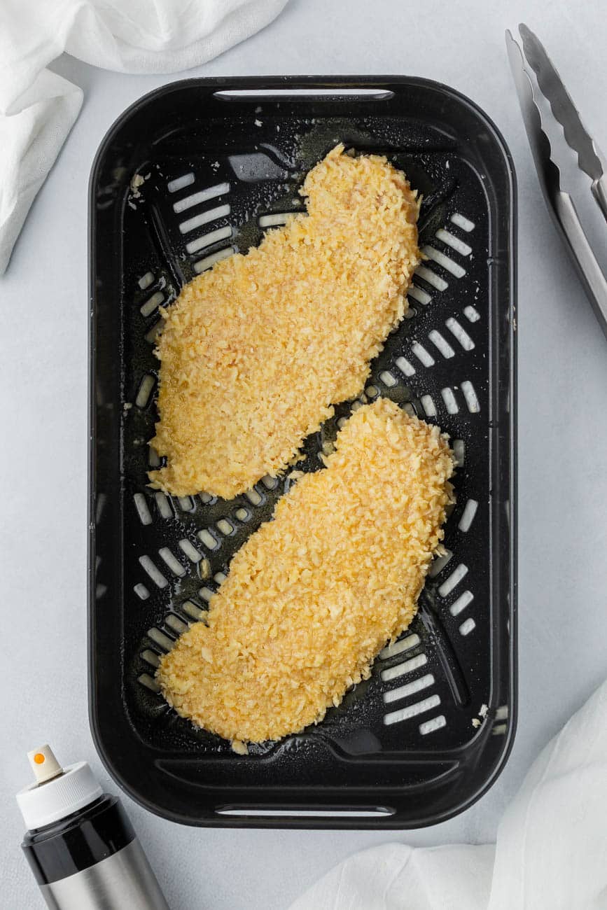 Panko crusted chicken cutlets in an air fryer basket.