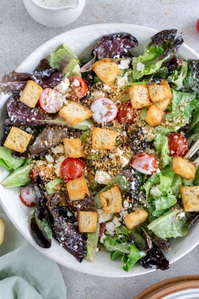 mixed greens salad with tomatoes and croutons in a large white salad bowl.