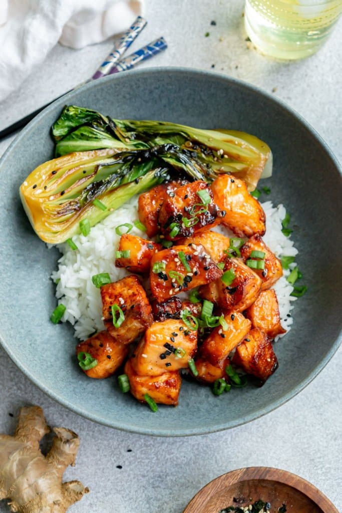 miso air fryer salmon bites in a blue bowl with bok choy and rice with a drink, chopsticks, and ginger on the side