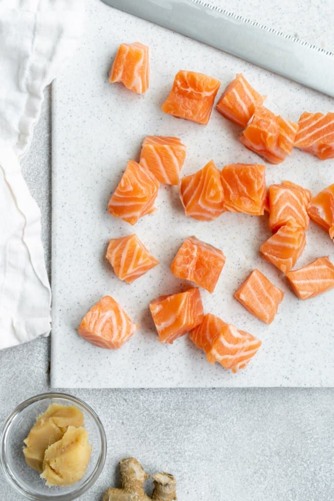 salmon cubes on a white cutting board with a knife