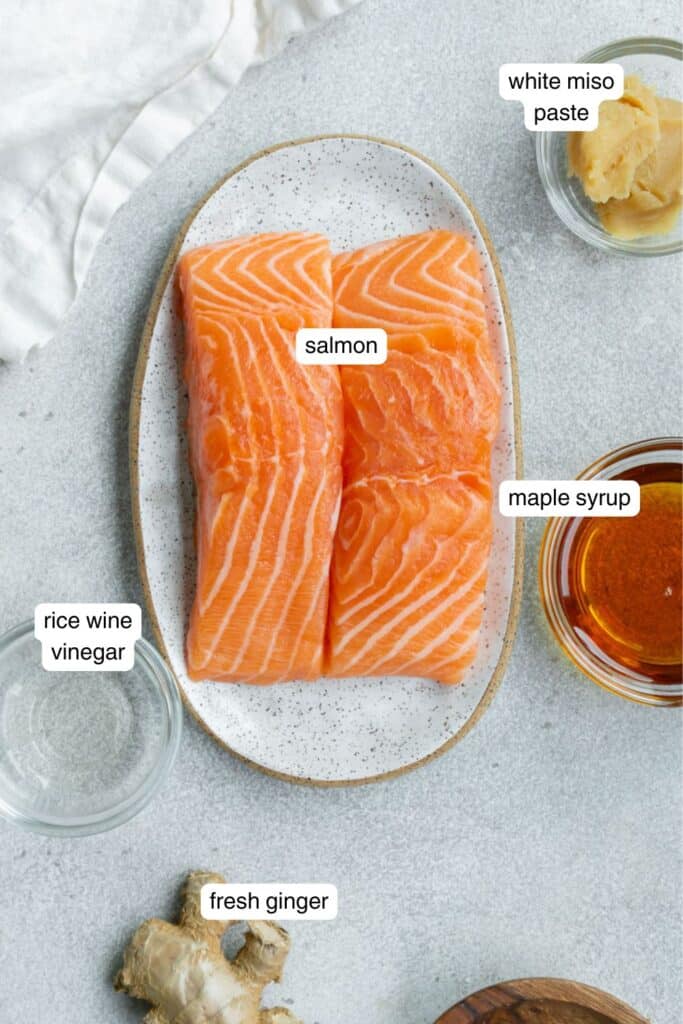 Salmon, white miso paste, maple syrup, and fresh ginger portioned on a table with a dish cloth on the side.