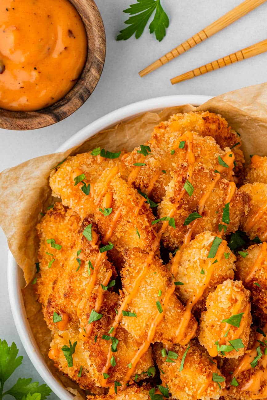 bang bang chicken in a white bowl with bang bang sauce on the side and chopsticks