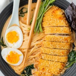 chicken katsu ramen in a black bowl with chopsticks and a soft boiled egg on top
